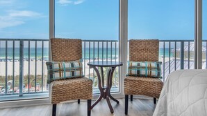 A balcony with wicker chairs and a small table, overlooking a beach with umbrellas and people. - Boardwalk 209 (Panama City Beach)