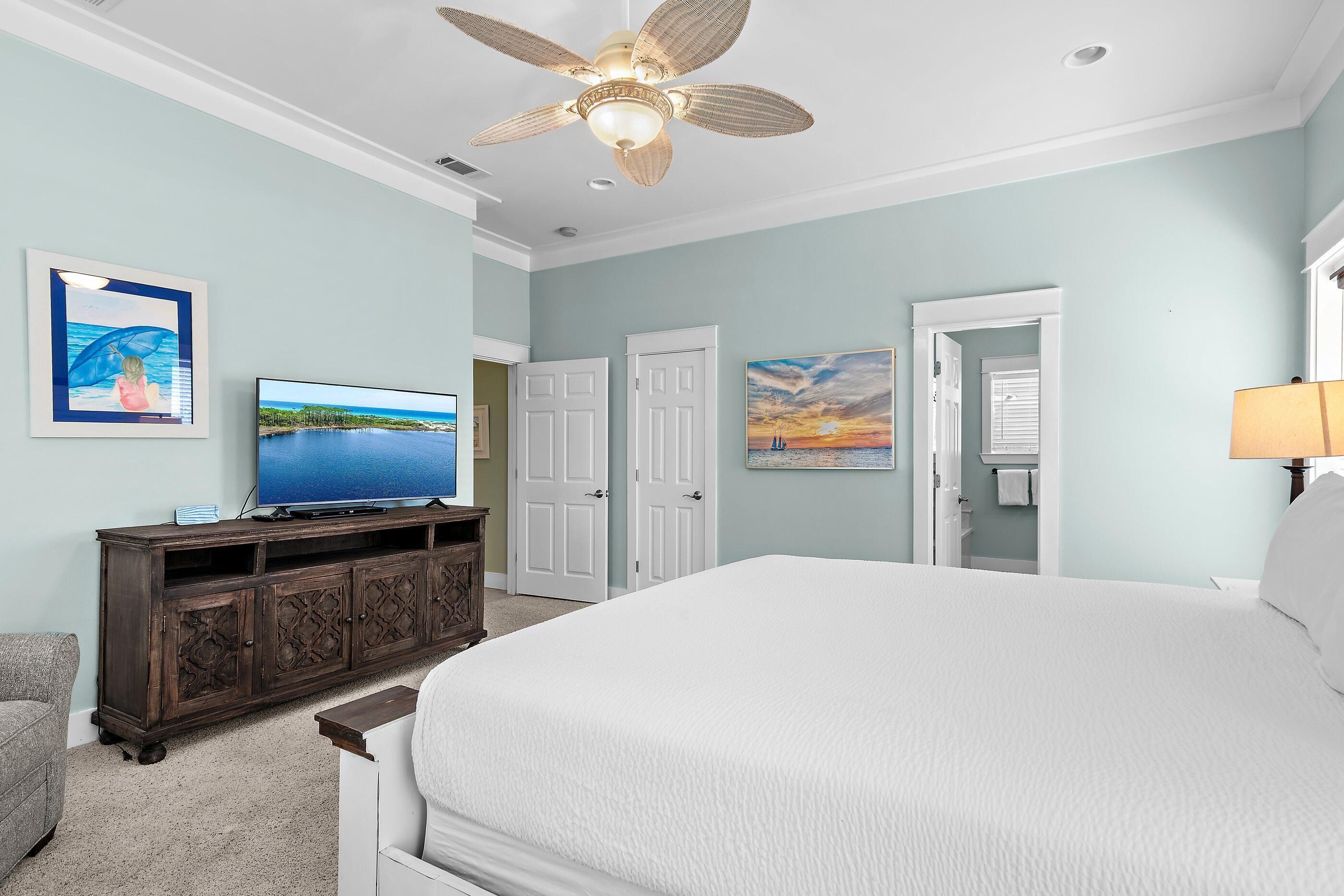 A bedroom with a bed, a television on a wooden cabinet, a ceiling fan, and two doors.