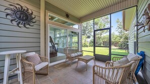 A covered patio with wicker furniture, a glass door leading to a backyard, and a sun-shaped wall decoration. - Drift Away (Santa Rosa Beach)