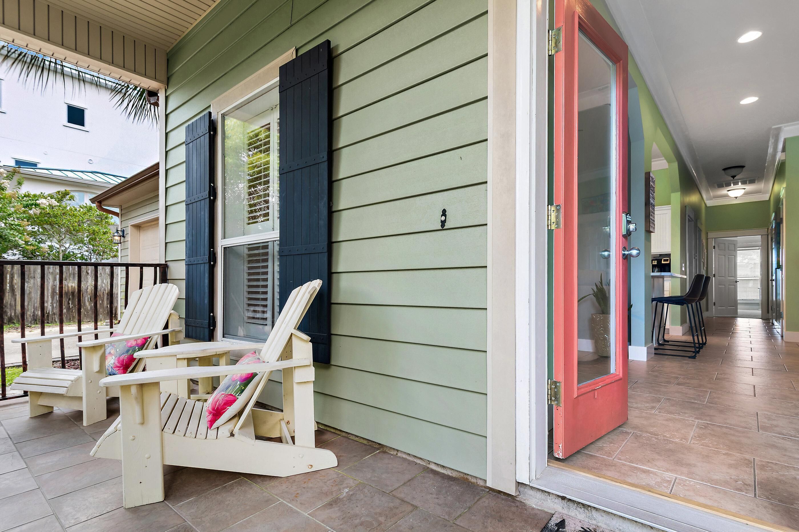 A porch with two Adirondack chairs and a red door leading to an interior space.