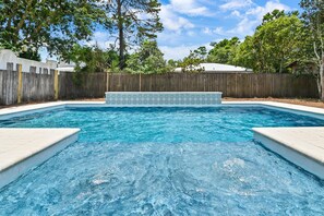 Une piscine entourée d’une clôture en bois, avec des arbres en arrière-plan.
