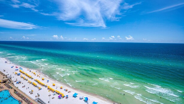 A beach with clear turquoise waters, a pool area, and beach umbrellas.