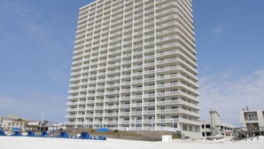 A tall, rectangular hotel with multiple balconies, located near a beach with some blue structures in the foreground.