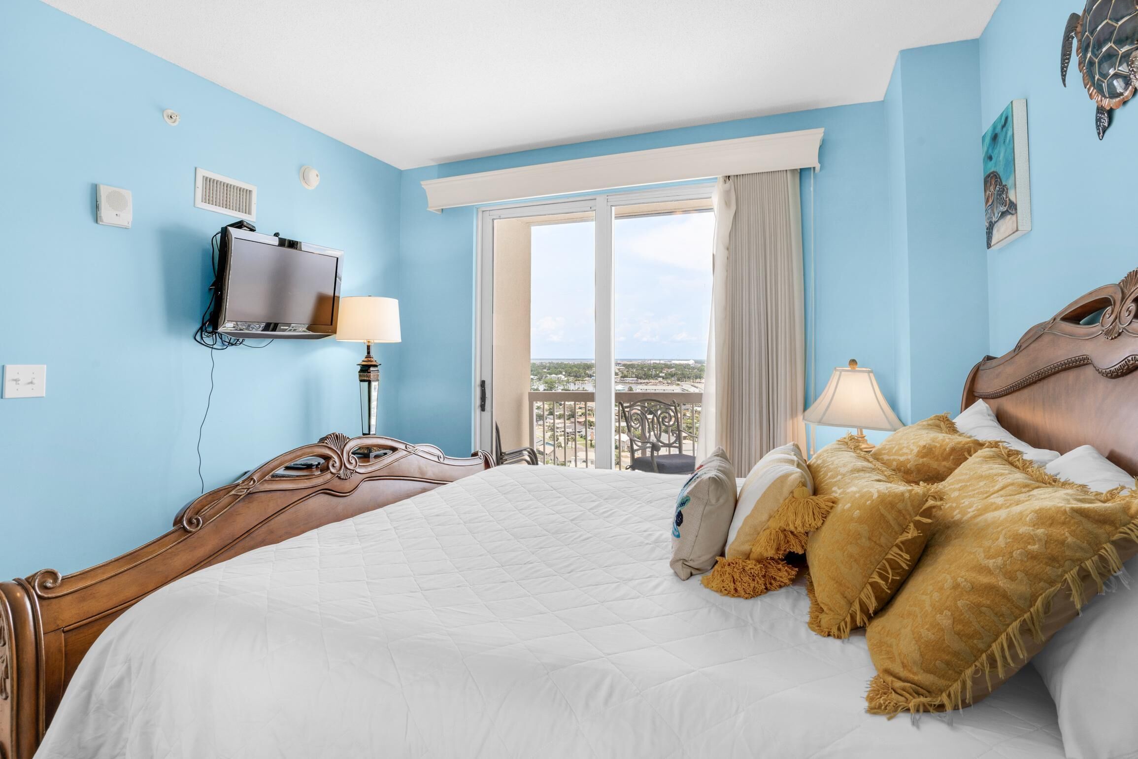 A hotel room with a large bed, a television mounted on the wall, and a balcony with a view.