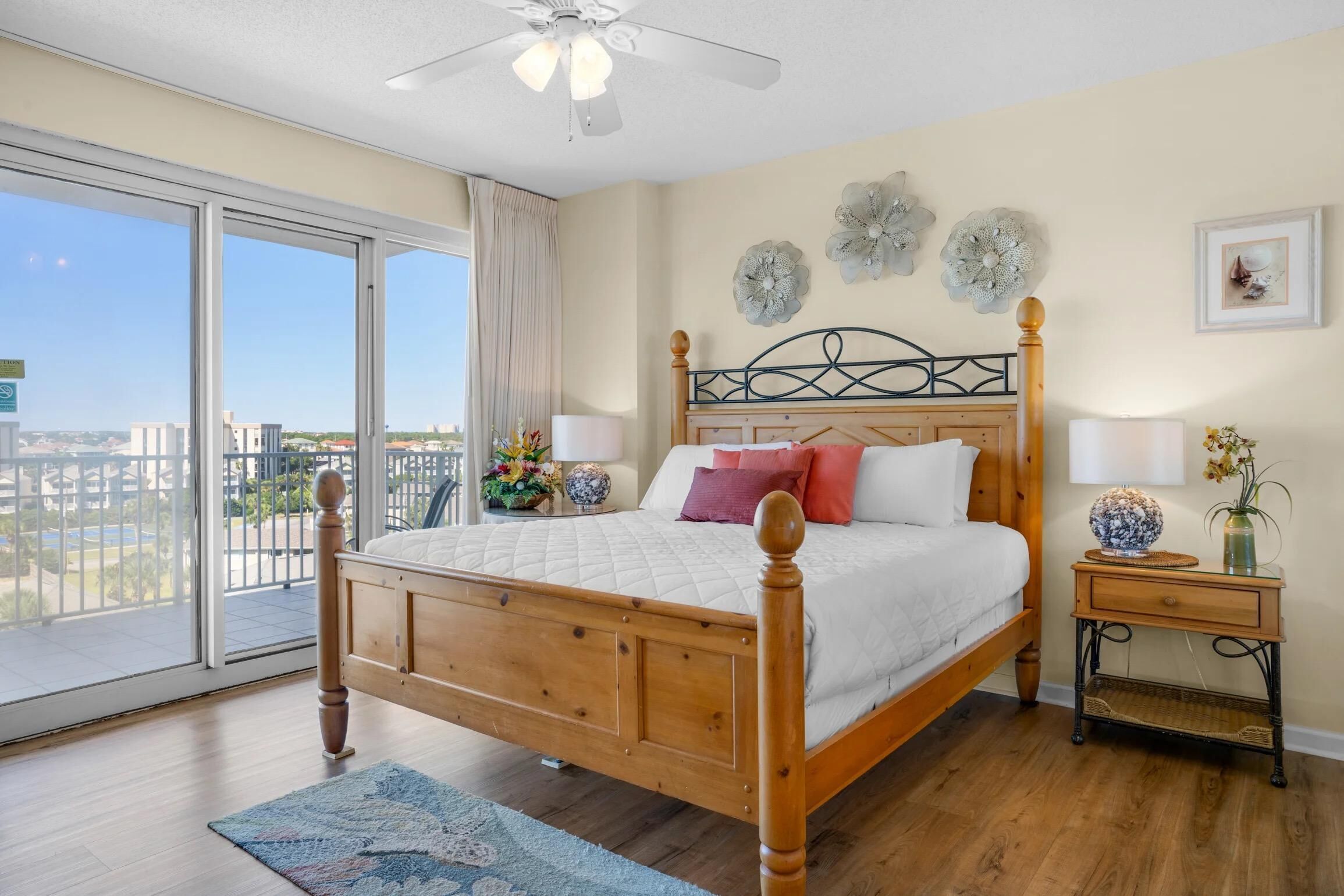 A bedroom with a wooden bed, a nightstand, a lamp, and a view of the city through large windows.