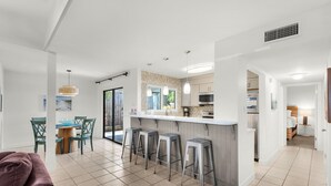 A modern kitchen with a central island, bar stools, and a dining area with chairs and a table. - Seascape 51A - Beach Baby (Miramar Beach)