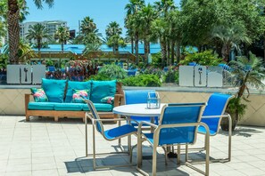 An outdoor seating area with a turquoise sofa and blue chairs, surrounded by palm trees and a view of a resort.