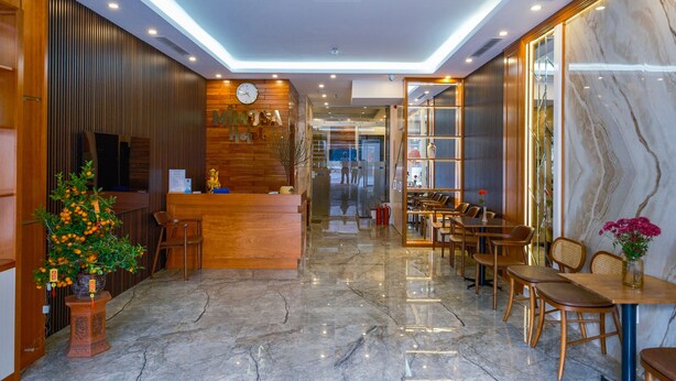 A hotel lobby with a reception desk, wooden paneling, a clock, and a seating area with tables and chairs. - MIMOSA HALONG HOTEL (Ha Long)
