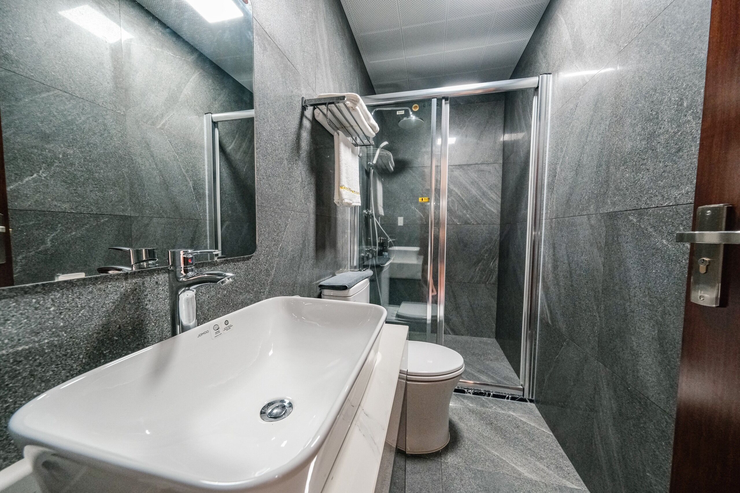 Un baño moderno con un lavamanos grande de color blanco, una cabina de ducha con mampara de vidrio y un inodoro.