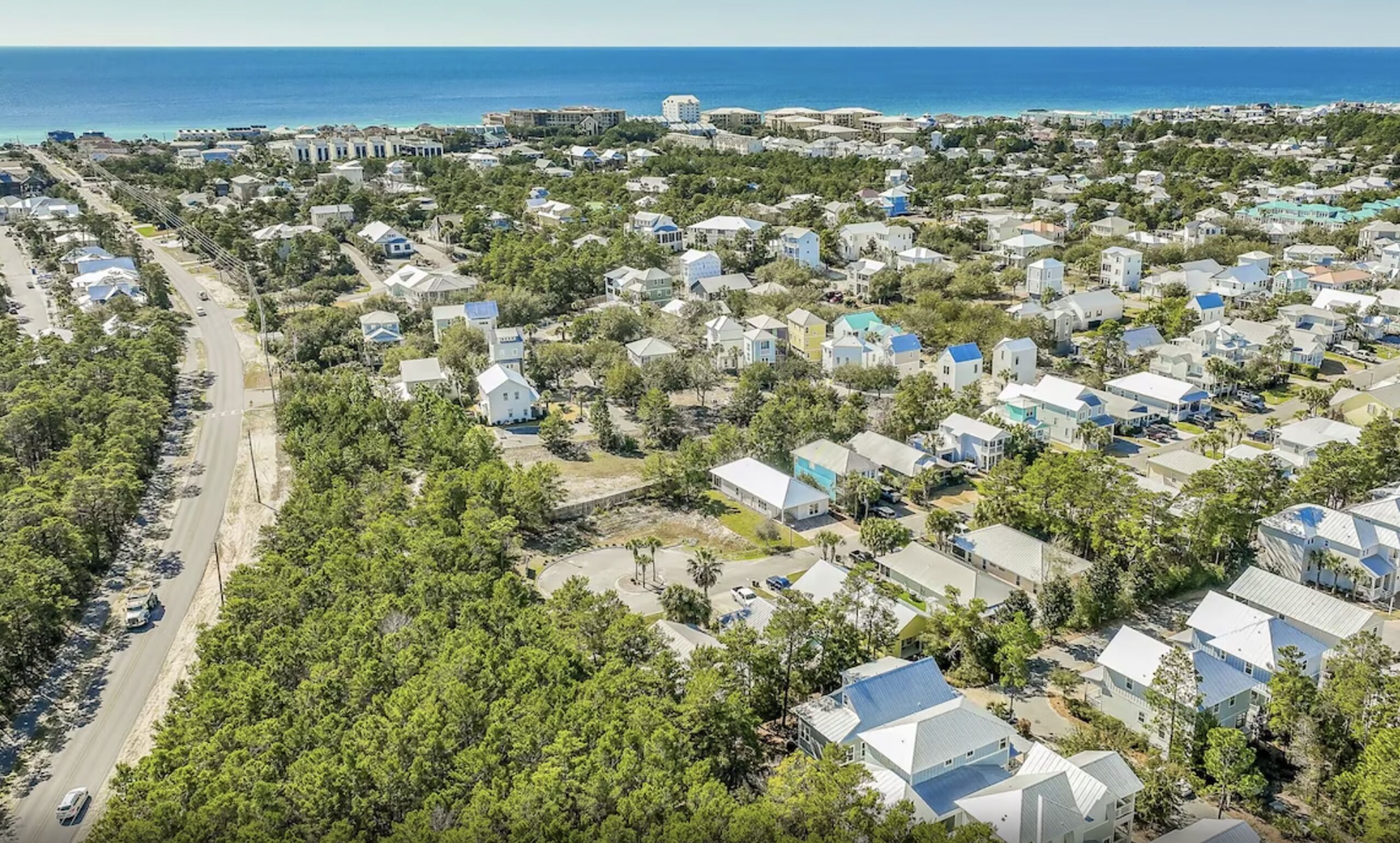 Vista aérea de uma área residencial costeira, com casas, uma estrada e uma praia ao fundo.
