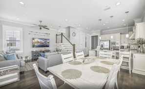 A spacious living room with a dining area, kitchen, and staircase. - Barefoot Blessing (Santa Rosa Beach)