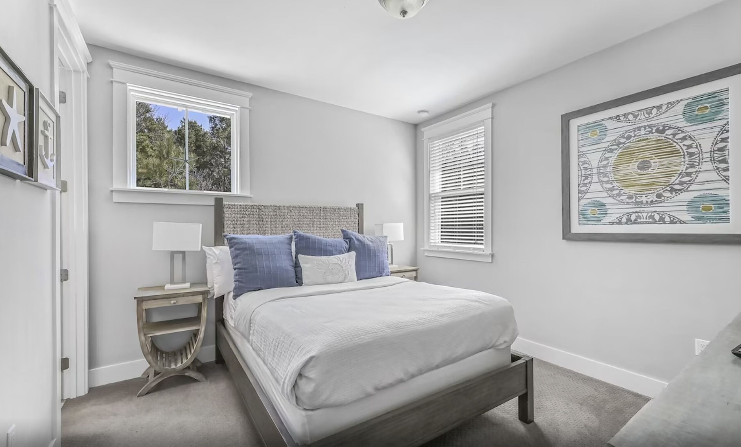A bedroom with a bed, two bedside tables, a window, and a wall-mounted artwork.
