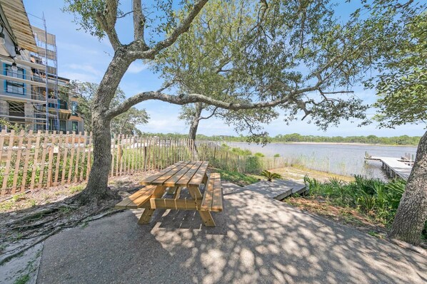 A wooden picnic table with benches, a paved walkway, and a view of a lake with a dock.