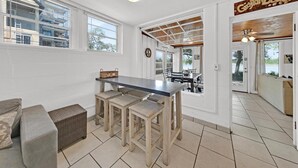 En rummelig stue med et stort spisebord, flere barstole, en sofa og udsigt til det fri.