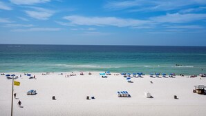 Une plage de sable blanc, avec une eau d’un bleu limpide et quelques parasols.