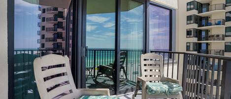 A balcony with two white chairs and a small table, overlooking a building and a clear sky.