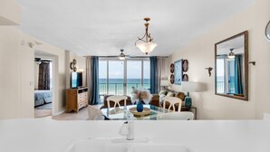 A spacious living area with a large window, a ceiling fan, and a dining table with chairs.