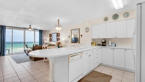A modern kitchen with white cabinets, a central island, and a view of the ocean through large windows.