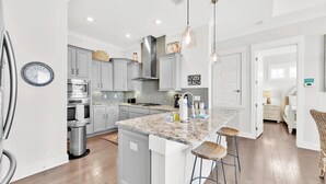 Una cocina moderna con armarios grises, una isla grande con taburetes de bar, electrodomésticos de acero inoxidable e iluminación colgante.