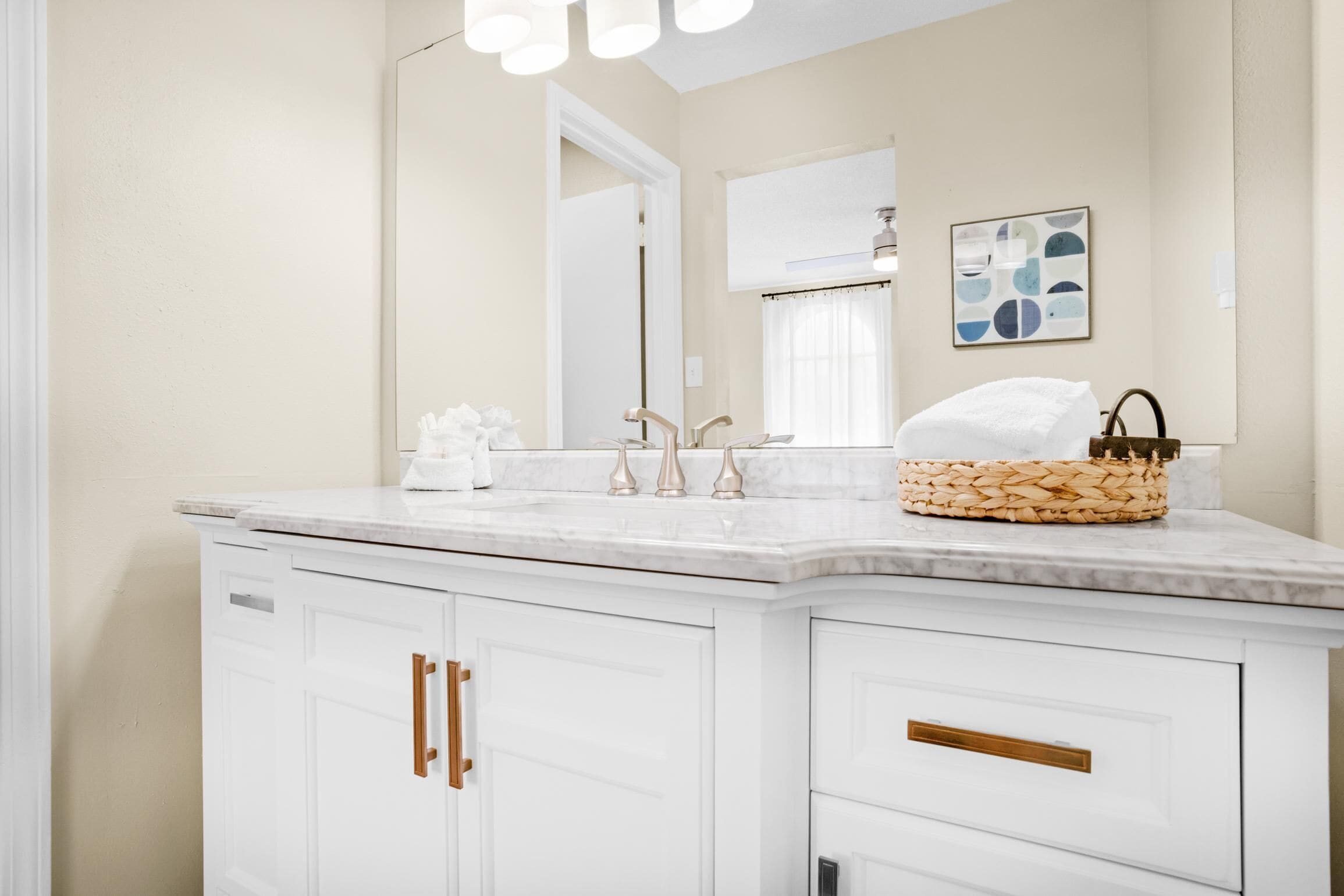 A modern bathroom with a white vanity, a large mirror, and a basket on the countertop.