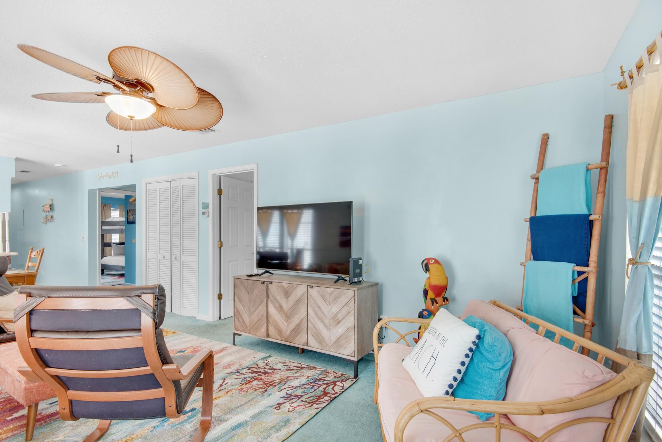 A room with a ceiling fan, a television, a wicker chair, a sofa, and a colorful rug.