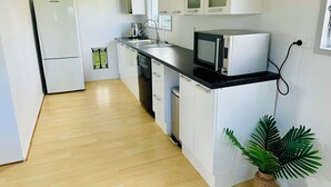 Una cocina compacta con armarios blancos, una encimera negra, un microondas, un refrigerador y un ventanal pequeño.