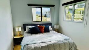 Un dormitorio con una cama grande, dos mesitas de noche, un ventanal con vistas a un jardín trasero y un cabecero.