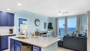 A modern kitchen with blue cabinets, a white island, and a dining area with a view of the ocean.