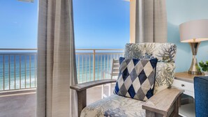A balcony with a view of the ocean, a chair with a patterned cushion, a lamp, and a small table.
