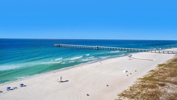 A beach with a pier extending into the ocean, sandy beach, and clear blue sky.