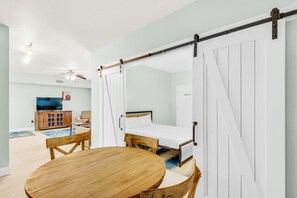 Quarto com cama, mesa de madeira, televisão e ventilador de teto.