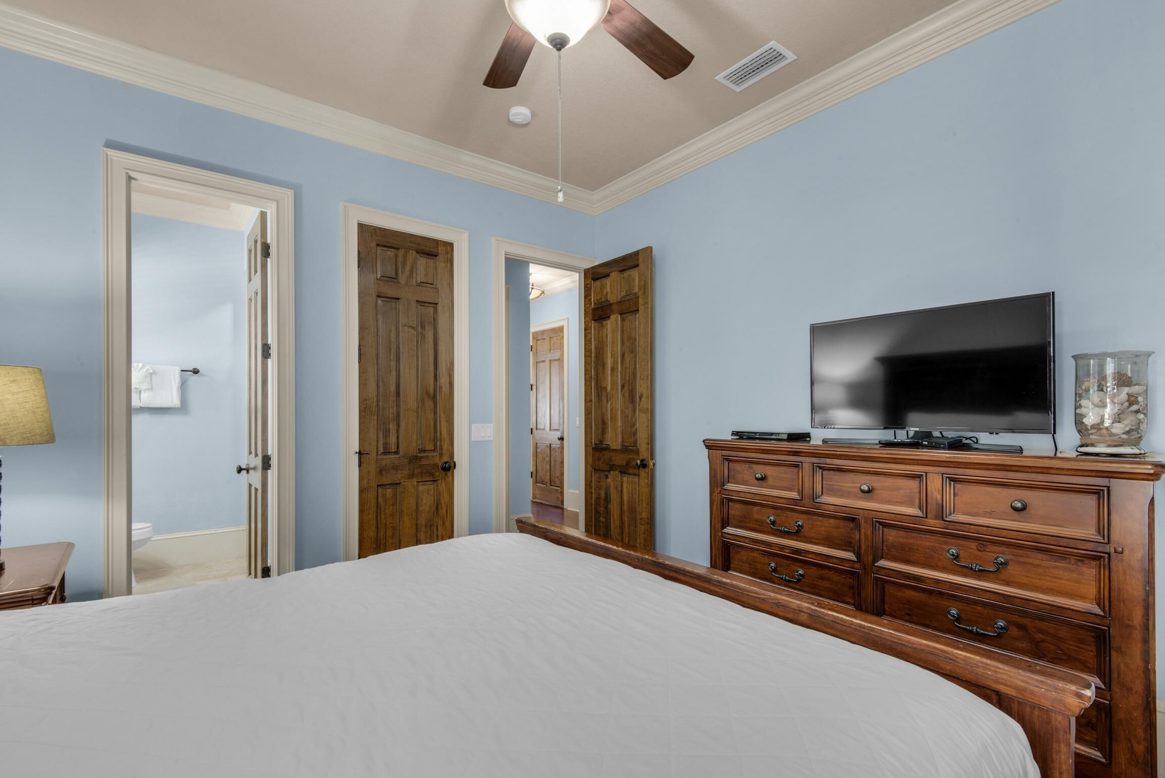 Une chambre à coucher avec un lit, une commode en bois, un téléviseur et un ventilateur de plafond.