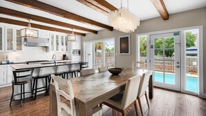 A spacious kitchen with wooden beams, a large island, and a dining area with a view of a swimming pool. - Casa Blanca (Destin)