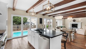 A modern kitchen with a large island, wooden beams, and a view of a swimming pool. - Casa Blanca (Destin)