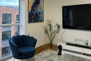 Uma sala de estar moderna com uma poltrona azul, uma televisão grande e uma planta.