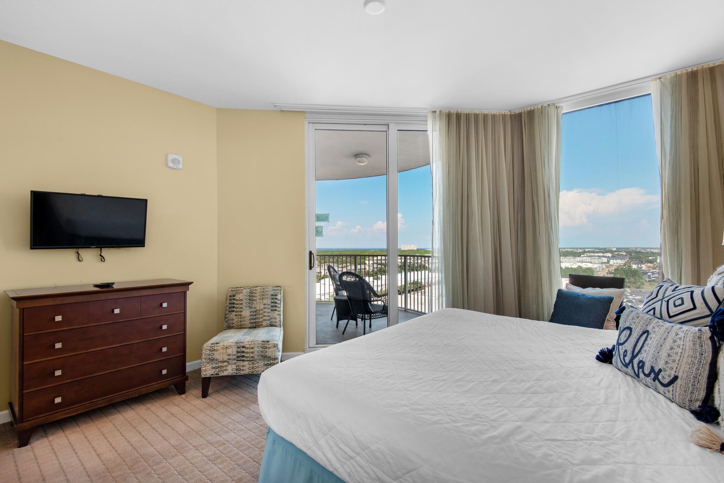 A hotel room with a large bed, a dresser, a television, a chair, and a balcony with a view.