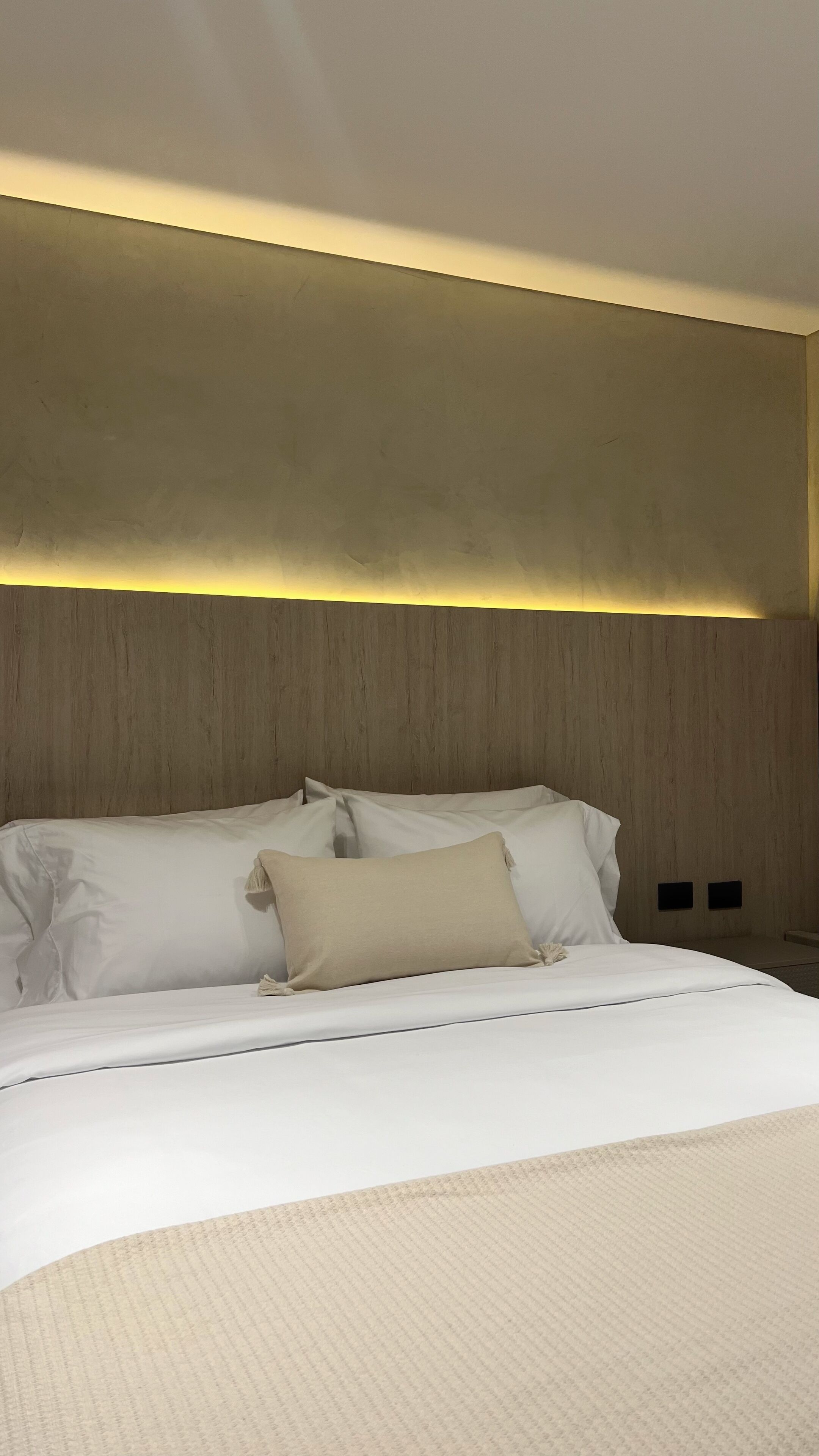 Une chambre d’hôtel moderne avec un grand lit, une tête de lit en bois et un luminaire fixé au mur.