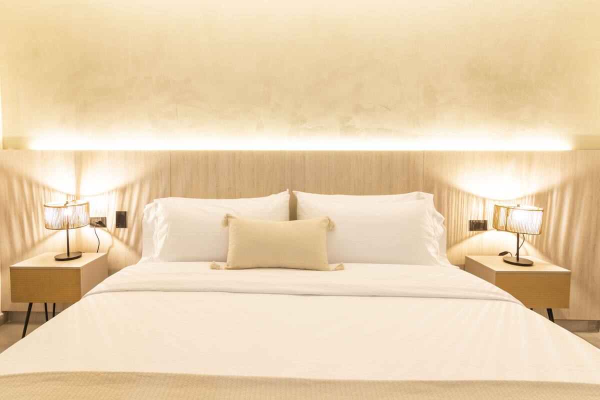 Una habitación de hotel con una cama grande, dos mesitas de noche con lámparas y un techo con textura.