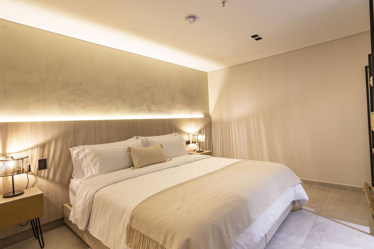 Un dormitorio moderno con una cama grande, lámparas de noche y una paleta de colores neutros.