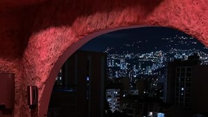 Zona de bar moderna con asientos iluminados en rojo y vistas a un paisaje urbano nocturno.