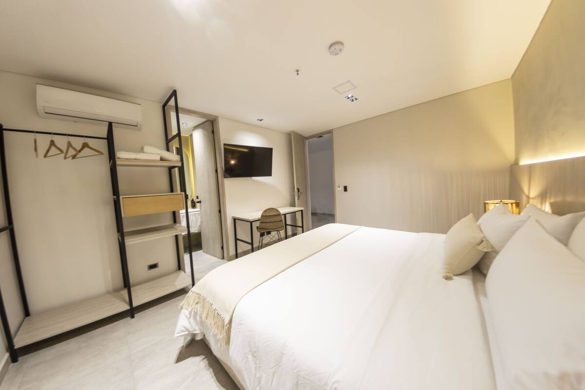 Una habitación de hotel con una cama grande, un escritorio, una silla y un televisor montado en la pared.