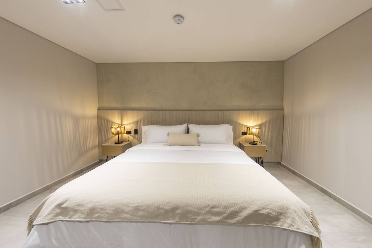 Un dormitorio con una cama grande, dos mesitas de noche con lámparas y una lámpara en el techo.