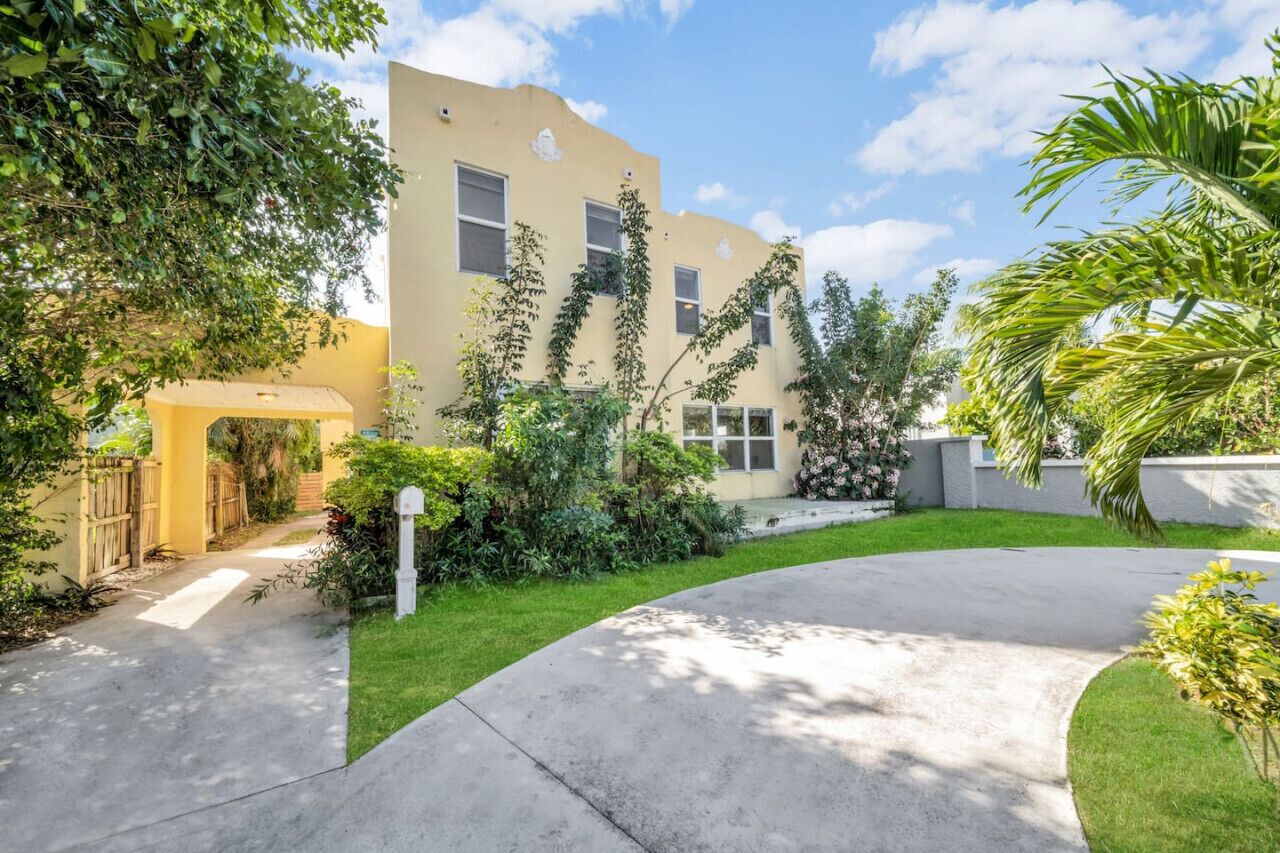 A residential building with a curved driveway, a gated entrance, and lush greenery.