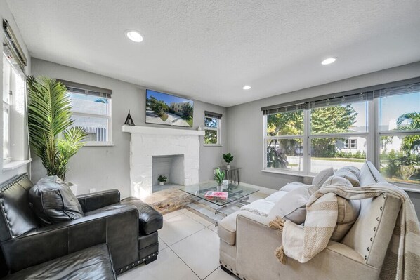 A modern living room with a fireplace, leather sofas, a glass coffee table, and large windows offering a view of the outdoors. - Spectacular Estate on Antique Row - Large Groups (West Palm Beach)
