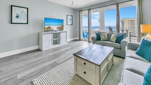 Una sala de estar moderna con una mesa de centro de madera, un sofá gris y un televisor sobre un mueble blanco.