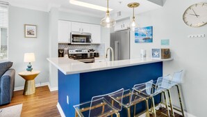 Una cocina moderna con una pared azul decorativa, electrodomésticos de acero inoxidable y una zona de bar con taburetes transparentes.