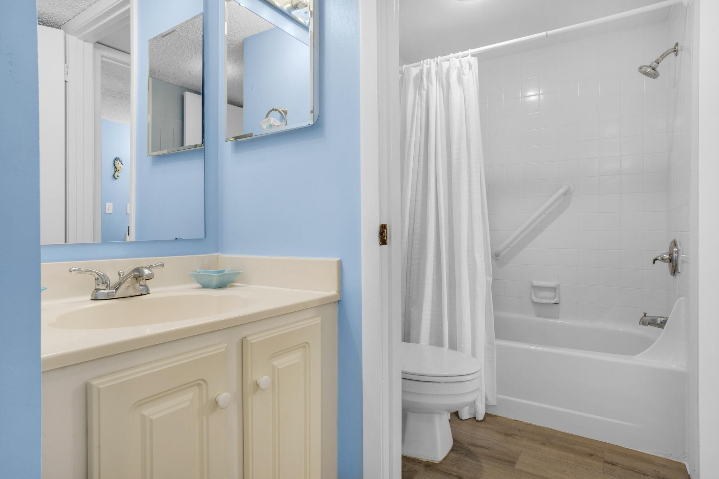Een badkamer met een wit bad, een wit toilet, een wastafel met een blauwe zeepbak en een spiegel.