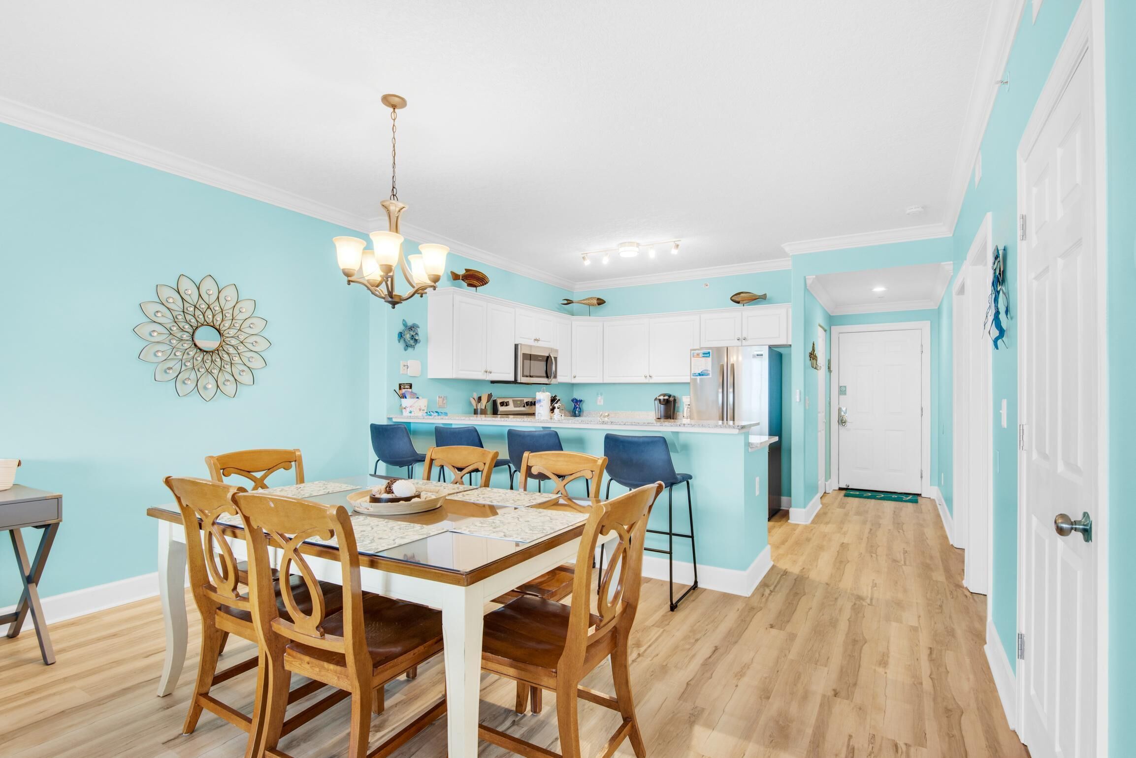 Un coin repas avec une table et des chaises en bois, une cuisine avec des meubles blancs et un mur d’accent bleu clair.