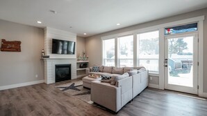 A spacious living room with a fireplace, a large sofa, and a view through a glass door.
