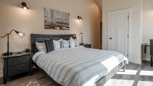 A bedroom with a bed, two bedside tables, a nightstand, a door, and a wall-mounted light fixture.